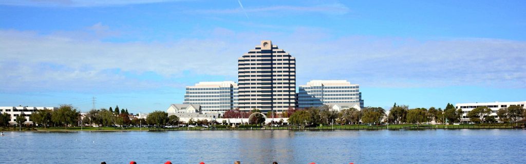 Foster City Website Design 3 Office buildings in Foster City rise behind a lake where people row under a blue sky.