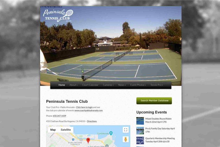 Two empty tennis courts with trees, clear sky, and a clubhouse in the background.