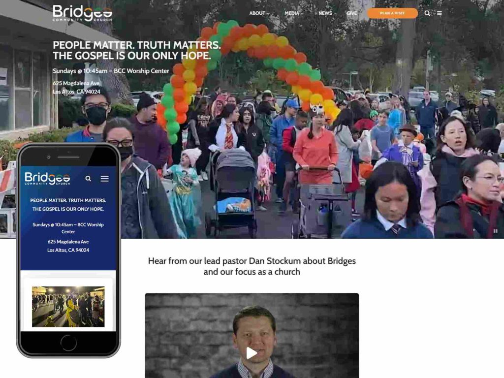 Bridges Community Church 8 Crowd at outdoor church event with colorful balloon arch; website info shown on phone.