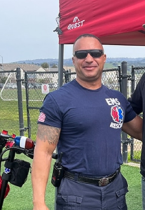 Web Accessibility Services 11 Man in EMS Rescue shirt and sunglasses standing outdoors near red tent and black fence.